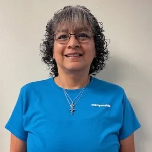 smiling woman with a blue merry maids uniform standing in front of a tan wall